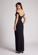 Back quarter image of a model wearing a black maxi dress, featuring off the shoulder short sleeves and a dipped back design. The dress featured is the Vesper Holland black maxi dress