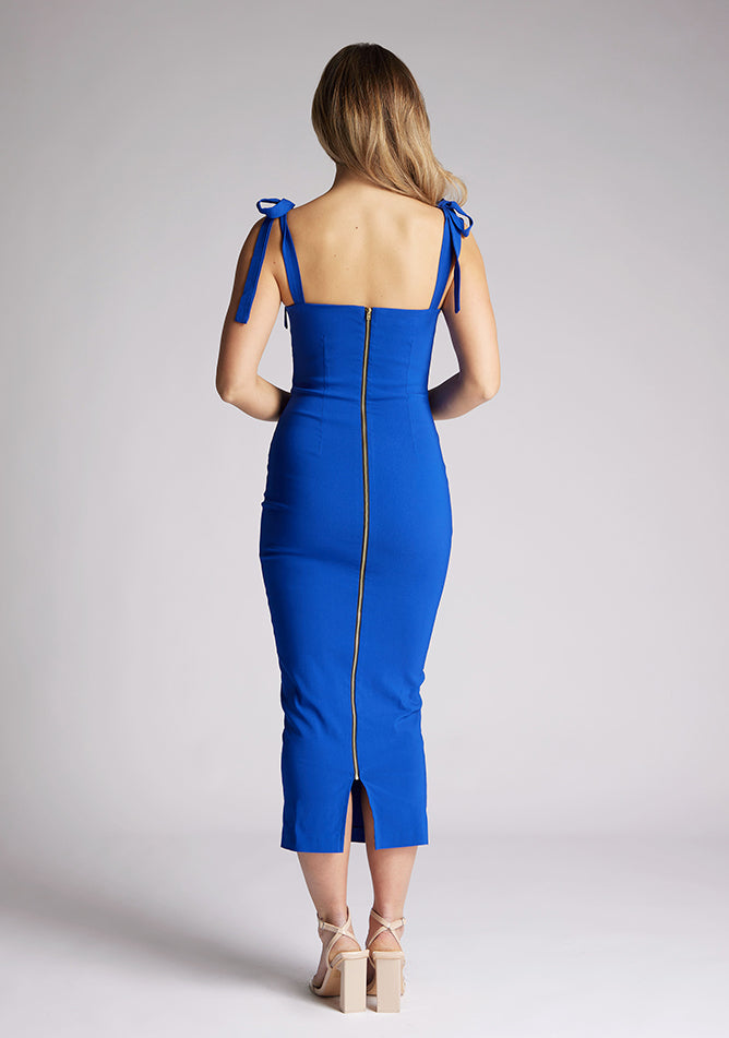 Back image of a model wearing a cobalt blue midaxi dress. The dress features a V cut out in the neck line and tie up straps. The dress featured is the Vesper Letty cobalt midaxi dress