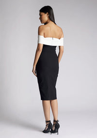 Back quarter image of a model wearing a off the shoulder midi dress, featuring a black body to the dress with a white band across the top and the arms. The dress featured is the Vesper Maricel monochrome midi dress