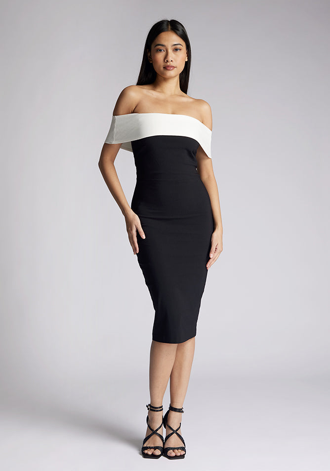 Front image of a model wearing a off the shoulder midi dress, featuring a black body to the dress with a white band across the top and the arms. The dress featured is the Vesper Maricel monochrome midi dress