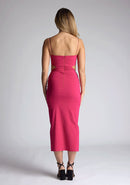 Back image of a model wearing a magenta midi dress, featuring cut outs at the waist and a front split in the skirt. The dress featured is the Vesper Marilynn magenta midaxi dress