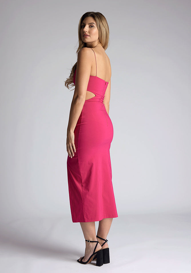 Back quarter image of a model wearing a magenta midi dress, featuring cut outs at the waist and a front split in the skirt. The dress featured is the Vesper Marilynn magenta midaxi dress