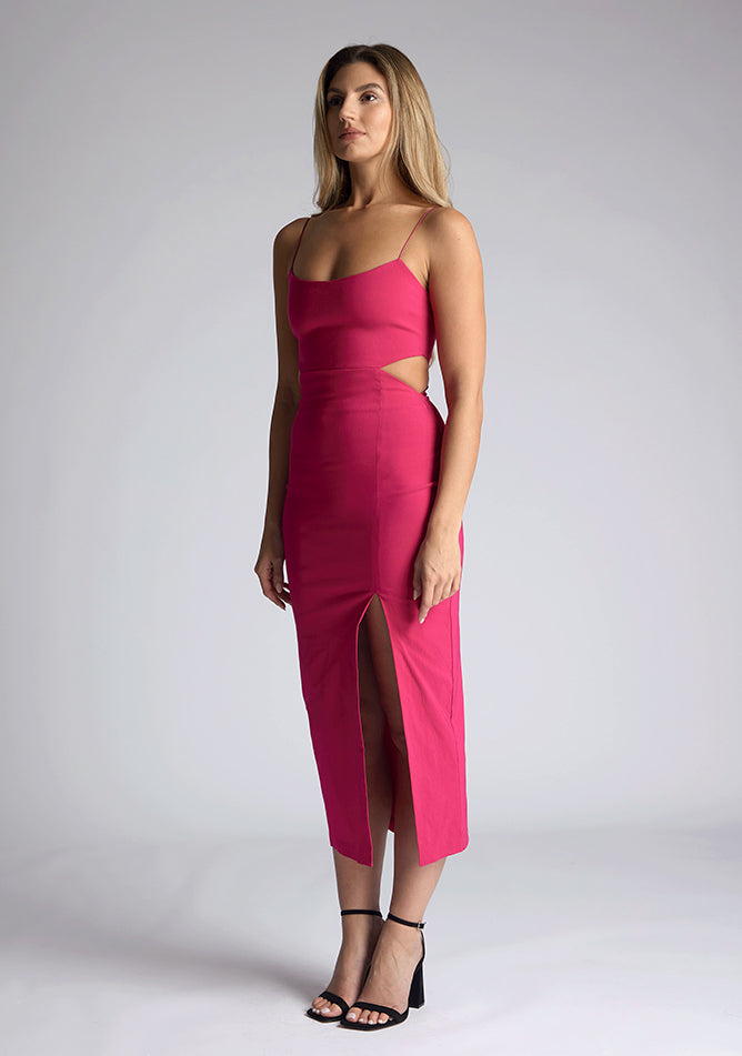 Front quarter image of a model wearing a magenta midi dress, featuring cut outs at the waist and a front split in the skirt. The dress featured is the Vesper Marilynn magenta midaxi dress