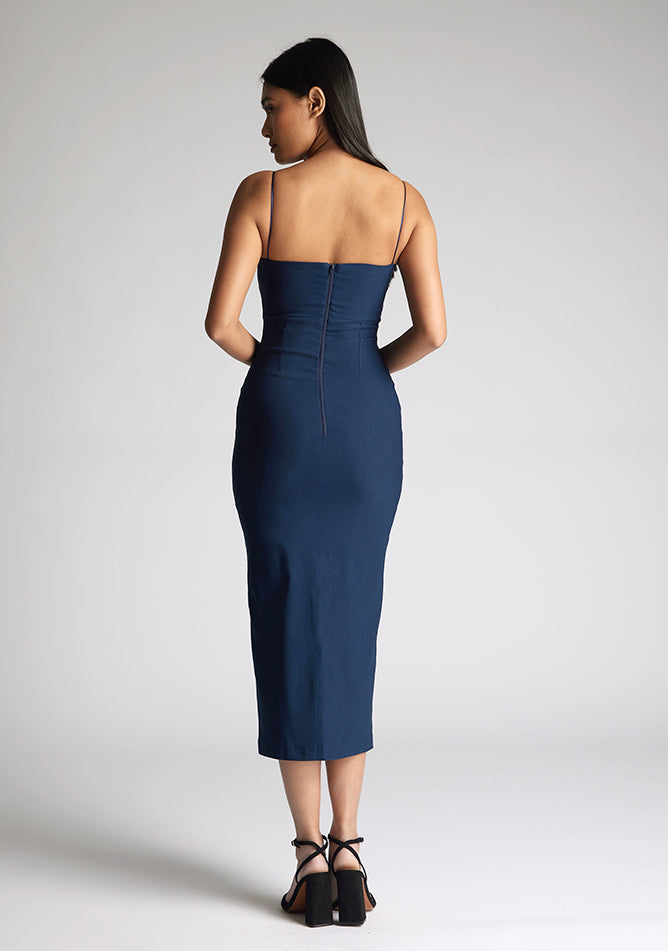 Back image of a model wearing a navy midaxi dress, featuring a sweetheart neckline and a front skirt split. The dress featured is the Vesper Miren navy midaxi dress