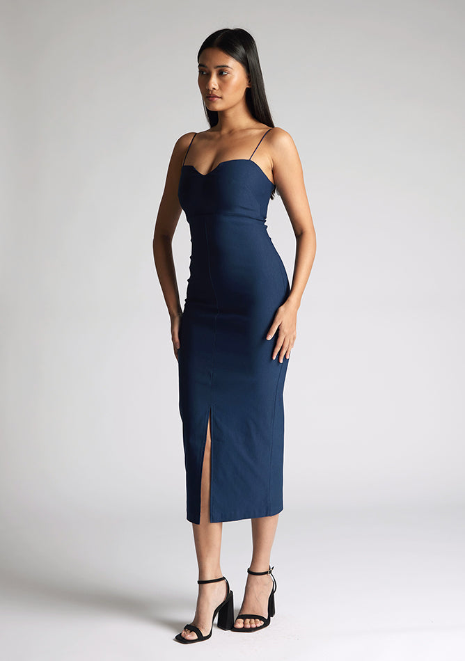 Front quarter image of a model wearing a navy midaxi dress, featuring a sweetheart neckline and a front skirt split. The dress featured is the Vesper Miren navy midaxi dress