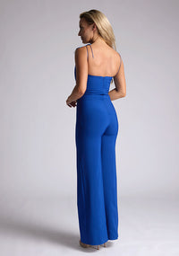 Back quarter image of a model wearing a royal blue jumpsuit, featuring a sweetheart neckline and tie up straps. The jumpsuit featured is the Vesper Nicole royal blue tie up jumpsuit