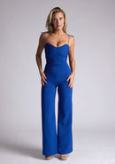 Front image of a model wearing a royal blue jumpsuit, featuring a sweetheart neckline and tie up straps. The jumpsuit featured is the Vesper Nicole royal blue tie up jumpsuit