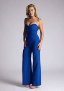 Front quarter image of a model wearing a royal blue jumpsuit, featuring a sweetheart neckline and tie up straps. The jumpsuit featured is the Vesper Nicole royal blue tie up jumpsuit