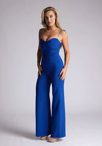 Front quarter image of a model wearing a royal blue jumpsuit, featuring a sweetheart neckline and tie up straps. The jumpsuit featured is the Vesper Nicole royal blue tie up jumpsuit