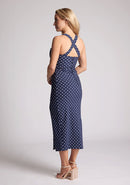 Back quarter image of a model wearing a navy polka dot midaxi dress, featuring a sweetheart neckline and straps that cross at the back. The dress featured is the Vesper Poppy navy polka dot sweetheart midaxi dress