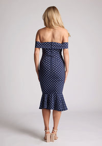 Back image of a model wearing a navy polka dot dress, featuring a bardot neckline and frill hem. The dress featured is the Vesper Racquel navy polka dot bardot midaxi dress