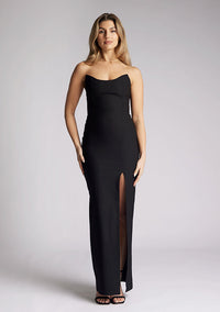 Front image of a model wearing a black maxi dress, with a strapless design and front skirt split. The dress featured is the Vesper Remington black maxi dress