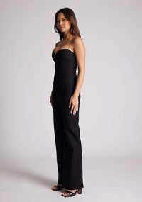 Front quarter image of a model wearing a black jumpsuit, featuring a sweetheart neckline and a wide leg design. The jumpsuit featured is the Vesper Rogan black jumpsuit