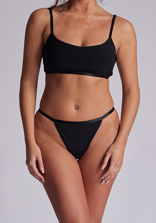 A front image of a model wearing a a black thong with thin sides. The thong featured is the Sapphire Everyday Comfort Thong and is worn with the Julia Everyday Comfort Bra
