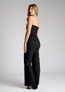 Back quarter image of a model wearing black wide leg trousers, featuring a high wist and a V cut out at the back. The trousers featured are the Vesper June black wide leg trousers and are worn with the Vesper Sharon black strapless top