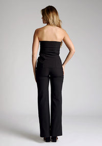 Back image of a model wearing a strapless black top, featuring an asymmetric hem and buckle detailing. The top featured is the Vesper Sharon black top worn with the Vesper June black wide leg trousers
