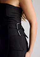Detail image of a model wearing a strapless black top, featuring an asymmetric hem and buckle detailing. The top featured is the Vesper Sharon black top worn with the Vesper June black wide leg trousers