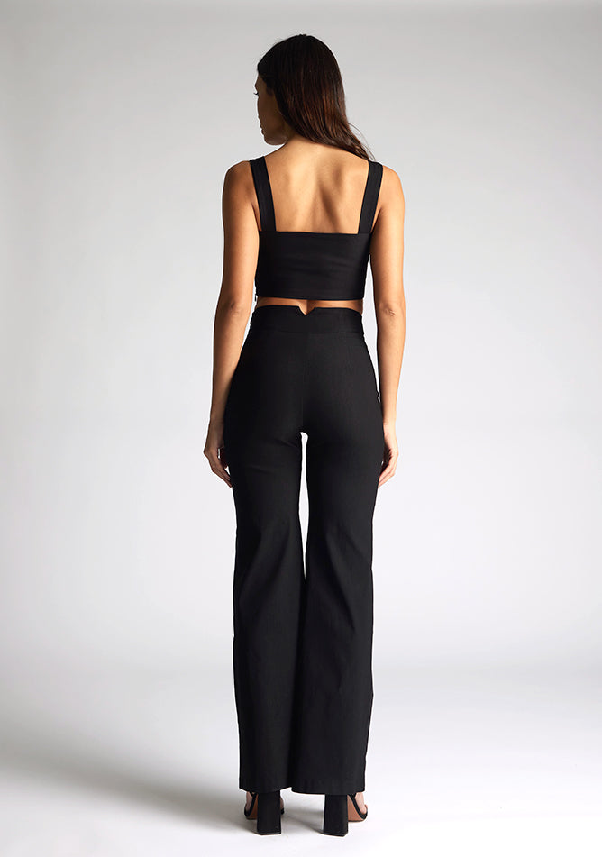 Back image of a model wearing a black crop top, featuring a sweetheart neckline and thick straps. The top featured is the Vesper Sky black crop top worn with Vesper June black wide leg trousers