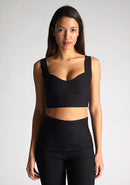 Close up image of a model wearing a black crop top, featuring a sweetheart neckline and thick straps. The top featured is the Vesper Sky black crop top worn with Vesper June black wide leg trousers