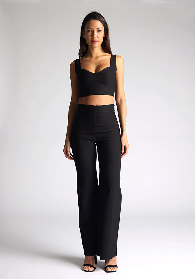 Front image of a model wearing a black crop top, featuring a sweetheart neckline and thick straps. The top featured is the Vesper Sky black crop top worn with Vesper June black wide leg trousers