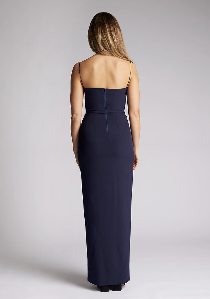Back image of a model wearing a navy maxi dress, featuring delicate straps and a front skirt split. The dress featured is the Vesper Tate navy maxi dress
