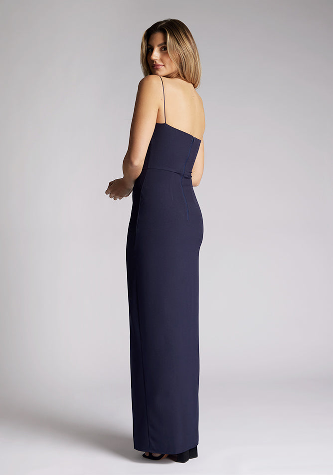 Back quarter image of a model wearing a navy maxi dress, featuring delicate straps and a front skirt split. The dress featured is the Vesper Tate navy maxi dress