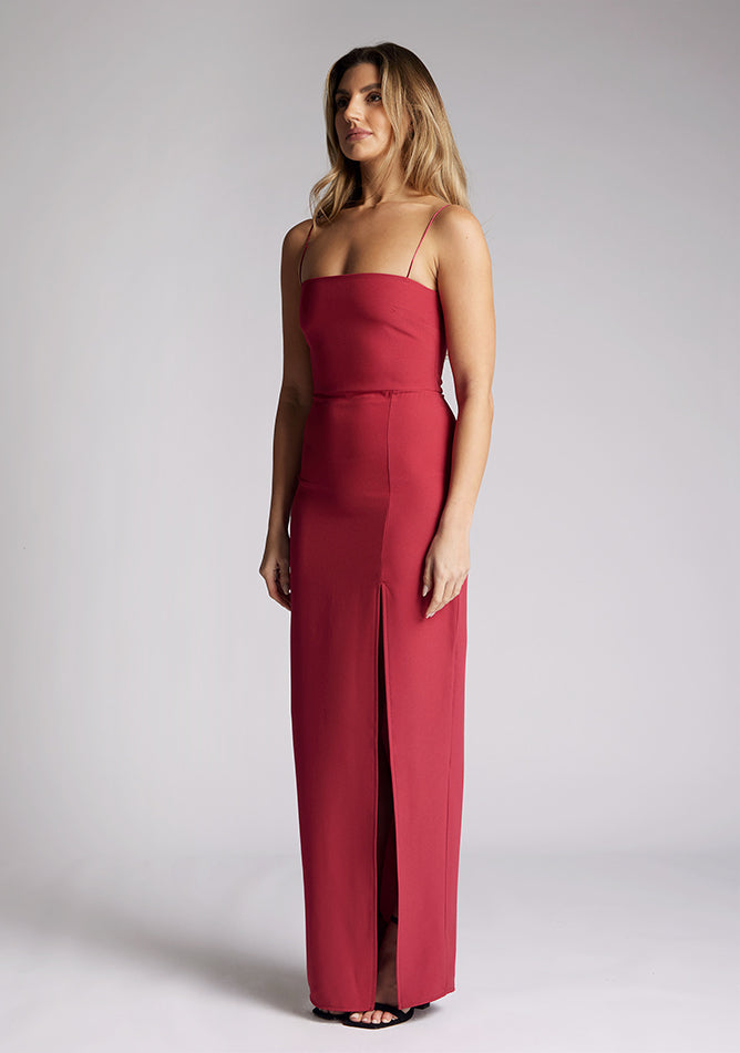 Front quarter image of a model wearing a raspberry maxi dress, featuring delicate straps and a front skirt split. The dress featured is the Vesper Tate raspberry maxi dress