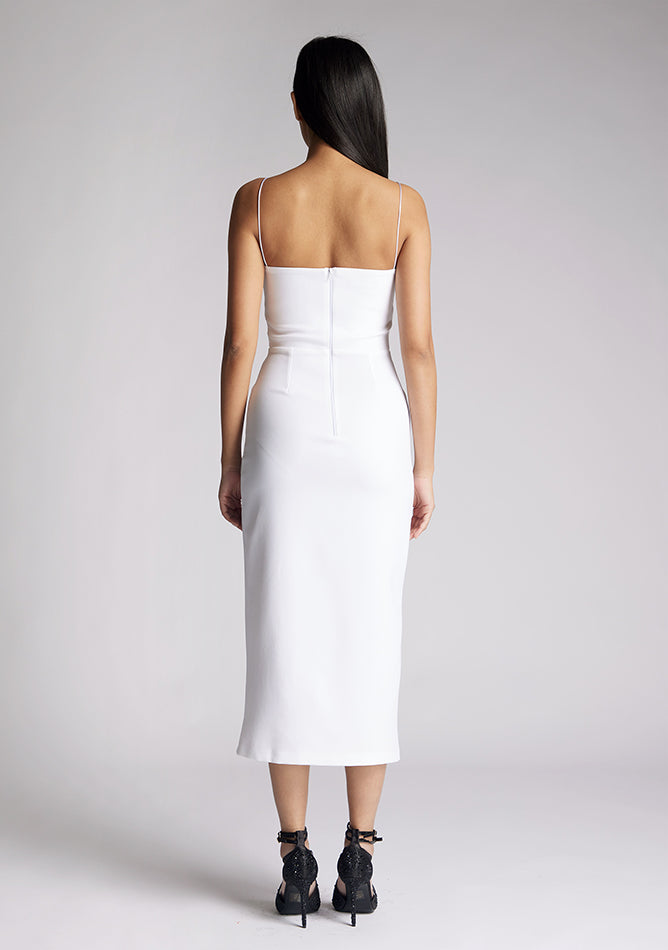 Back image of a model wearing a white midaxi dress, featuring delicate straps and a front skirt split. The dress featured is the Vesper Tate white midaxi dress