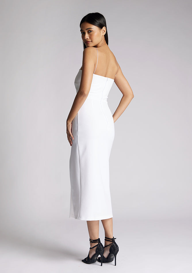 Back quarter image of a model wearing a white midaxi dress, featuring delicate straps and a front skirt split. The dress featured is the Vesper Tate white midaxi dress