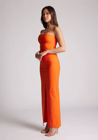 Front quarter image of a model wearing an orange strapless maxi dress with a front split and centre back zip. The design featured is the Vesper Alaya Orange Bodycon Maxi Dress.