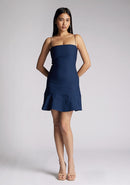 Front image of a model wearing a navy mini dress with a straight neckline, thin straps, a fitted bodice and flared ruffle hem with invisible centre back zip. The design featured is the Vesper Brenda Navy Mini Dress
