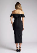 Back image of a model wearing a black midaxi dress, featuring a bardot neckline with a ruffle design, front skirt split and invisible centre back zip. The style featured is Vesper Deirdre Black Midaxi Dress.