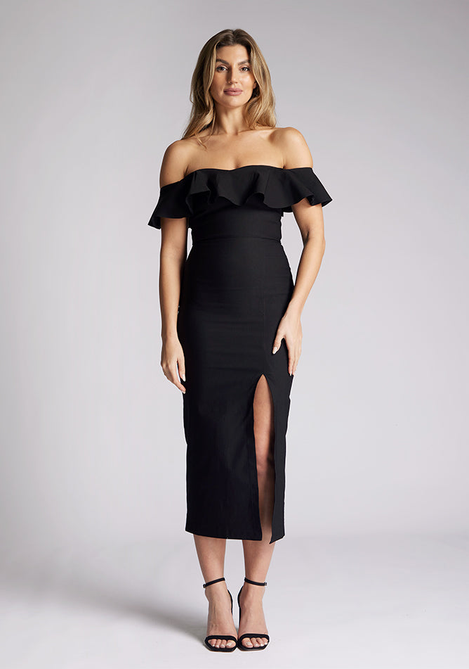 Front image of a model wearing a black midaxi dress, featuring a bardot neckline with a ruffle design, front skirt split and invisible centre back zip. The style featured is Vesper Deirdre Black Midaxi Dress.