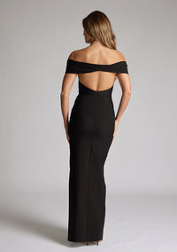 Back image of model wearing a black maxi dress with a off-shoulder design for a sophisticated touch, a front skirt split adds a subtle allure. The design featured is the Vesper Delta Black Maxi Dress.