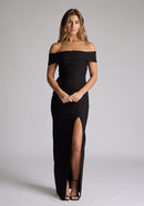 Front image of model wearing a black maxi dress with a off-shoulder design for a sophisticated touch, a front skirt split adds a subtle allure. The design featured is the Vesper Delta Black Maxi Dress.