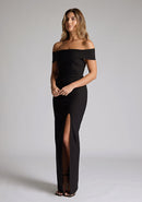 Front quarter image of model wearing a black maxi dress with a off-shoulder design for a sophisticated touch, a front skirt split adds a subtle allure. The design featured is the Vesper Delta Black Maxi Dress.