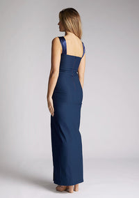 Back quarter image of a model wearing navy maxi dress with a chic neckline, sleeveless silhouette, figure-hugging body con design and satin panel at the top which twists up into straps. The design featured is the Vesper Fame Navy Maxi Dress