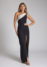 Front image of a brunette model wearing a monochrome dress in a maxi length with a one shoulder 
Front image of a brunette model wearing a monochrome dress in a maxi length with a asymmetric neckline, an ivory satin band across the neckline, thigh-high leg split and figure-hugging stretch crepe fabric with a white band across neckline. The design featured is the Vesper Fliss Monochrome Maxi Dress