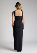 Back image of a model wearing a black maxi dress with a featuring  front split and one shoulder strap with another going across the neck. The design featured is the Vesper Gizelle black maxi dress