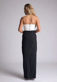 Back image of a model wearing a black and white maxi dress, featuring a subtle sweetheart neckline, thin halter neck straps, a small keyhole cut-out at bust and a front skirt split in the middle. This maxi dress showcases an elegant ivory bust with a black maxi, the style featured is Vesper Heather Monochrome Maxi Dress.