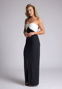 Quarter front image of a model wearing a black and white maxi dress, featuring a subtle sweetheart neckline, thin halter neck straps, a small keyhole cut-out at bust and a front skirt split in the middle. This maxi dress showcases an elegant ivory bust with a black maxi, the style featured is Vesper Heather Monochrome Maxi Dress.