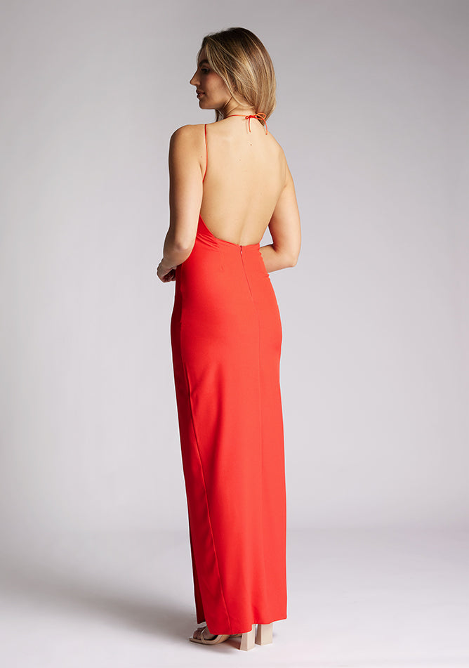 Quarter back image of a model wearing a red halter neck maxi dress, featuring a keyhole cut out and a front skirt split. The dress featured is the Vesper Ivie red maxi dress