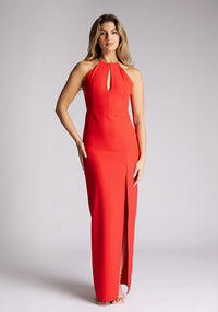 Front image of a model wearing a red strappy maxi dress with a halter neckline with a chic back fastening and subtle keyhole detail, its backless design exudes refinement and front skirt split. The design featured is the Vesper Ivie Red Strappy Maxi Dress
