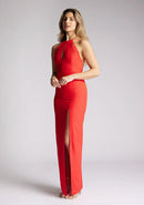 Front quarter image of a model wearing a red strappy maxi dress with a halter neckline with a chic back fastening and subtle keyhole detail, its backless design exudes refinement and front skirt split. The design featured is the Vesper Ivie Red Strappy Maxi Dress