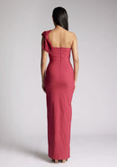 Back image of a model wearing a raspberry maxi dress, featuring an asymmetric neckline, one shoulder with statement bow detail and a front skirt split. The dress featured is Vesper Keegan Raspberry One Shoulder Maxi Dress