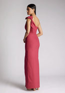 Back quarter image of a model wearing a raspberry maxi dress, featuring an asymmetric neckline, one shoulder with statement bow detail and a front skirt split. The dress featured is Vesper Keegan Raspberry One Shoulder Maxi Dress