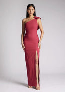 Front image of a model wearing a raspberry maxi dress, featuring an asymmetric neckline, one shoulder with statement bow detail and a front skirt split. The dress featured is Vesper Keegan Raspberry One Shoulder Maxi Dress