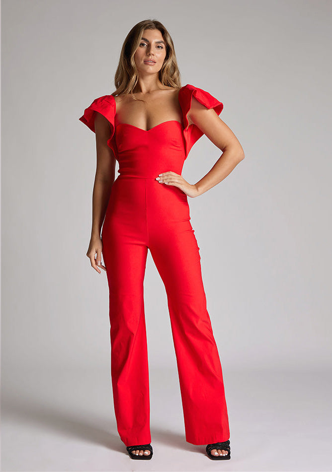 Front image of blonde model wearing a Red Jumpsuit with a  ruffled sleeves adding a touch of playfulness, a charming sweetheart neckline, and a convenient back zip, this outfit exudes timeless sophistication. The wide-leg design offers comfort and style, a design features Vesper Leigh Red Wide Leg Jumpsuit