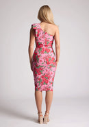 Back image of a model wearing a pink floral print midi dress, featuring an asymmetric neckline and one shoulder with a statement bow detail. The dress featured is the Vesper London Pink Floral One Shoulder Midi Dress.