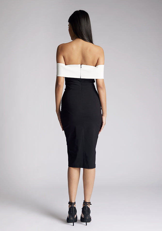 Back image of a model wearing a off the shoulder midi dress, featuring a black body to the dress with a white band across the top and the arms. The dress featured is the Vesper Maricel Monochrome Midi Dress